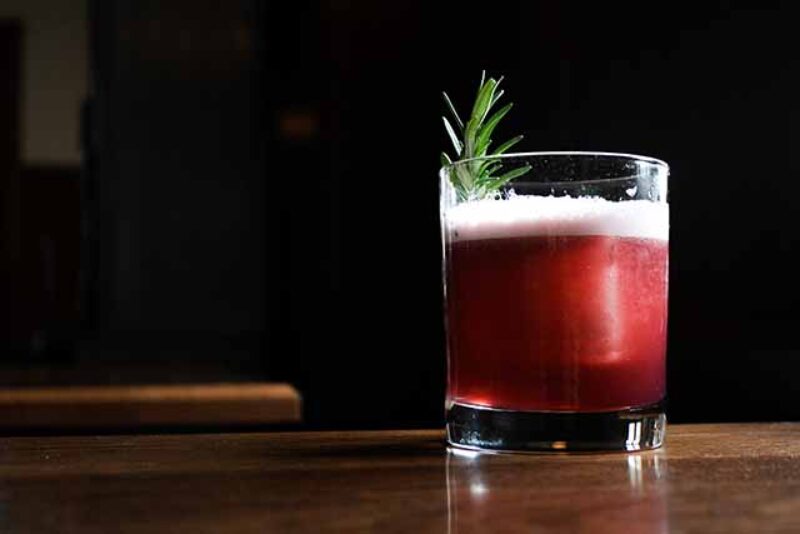 A red cocktail in a rocks glass from Glorietta, with a rosemary garnish.