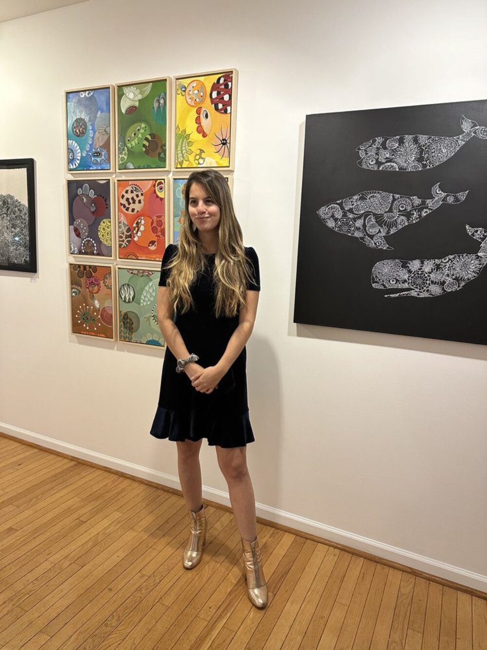 Artist Kara Bella posing next to her artwork in a gallery.