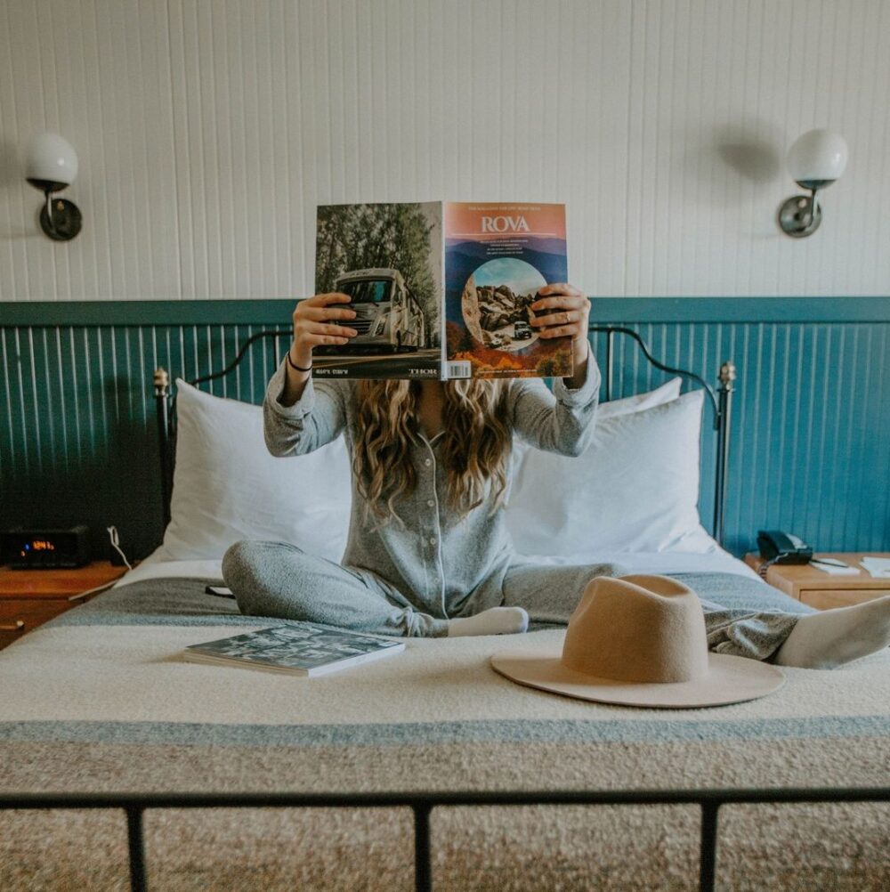 A girl reading a magazine on a bed in a hotel room.