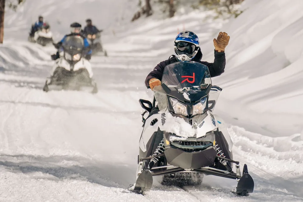 A snowmobiler waving in the snow.
