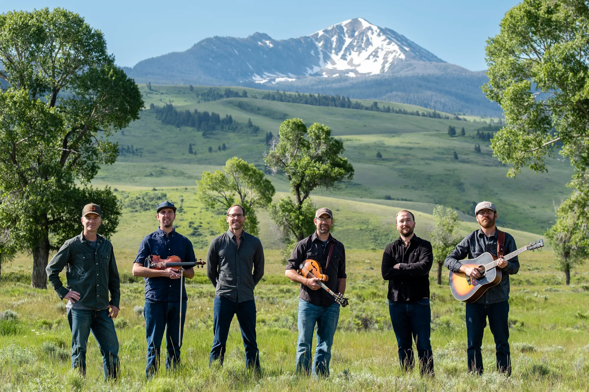 An album cover for the One Ton Pig artists in a green meadow with the mountains in the background.