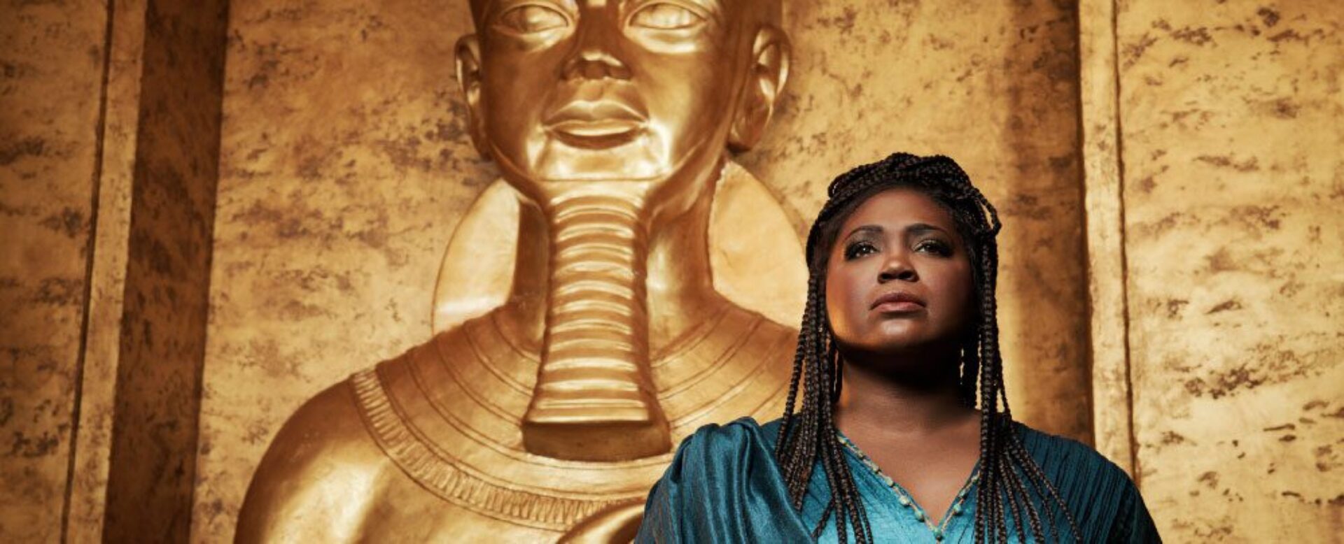Soprano Angel Blue in a blue gown, in front of a gold Egyptian god.