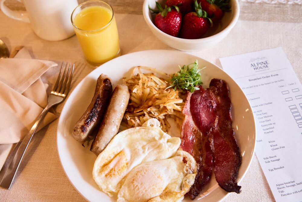 Two sausages, fried eggs, bacon, hashbrowns with a bowl of fresh berries and a glass of orange juice.
