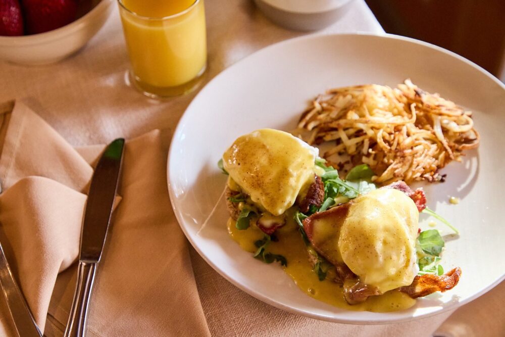 Eggs Benedict with a side of hash browns and a glass of orange juice at The Alpine House.