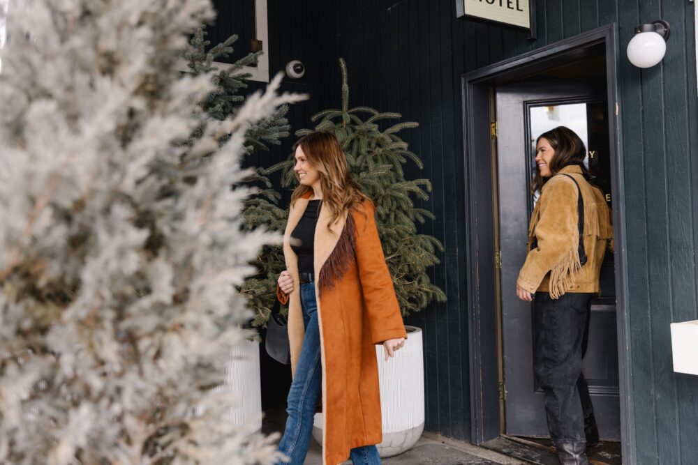 Two women walking out of the hotel entrance in long coats.