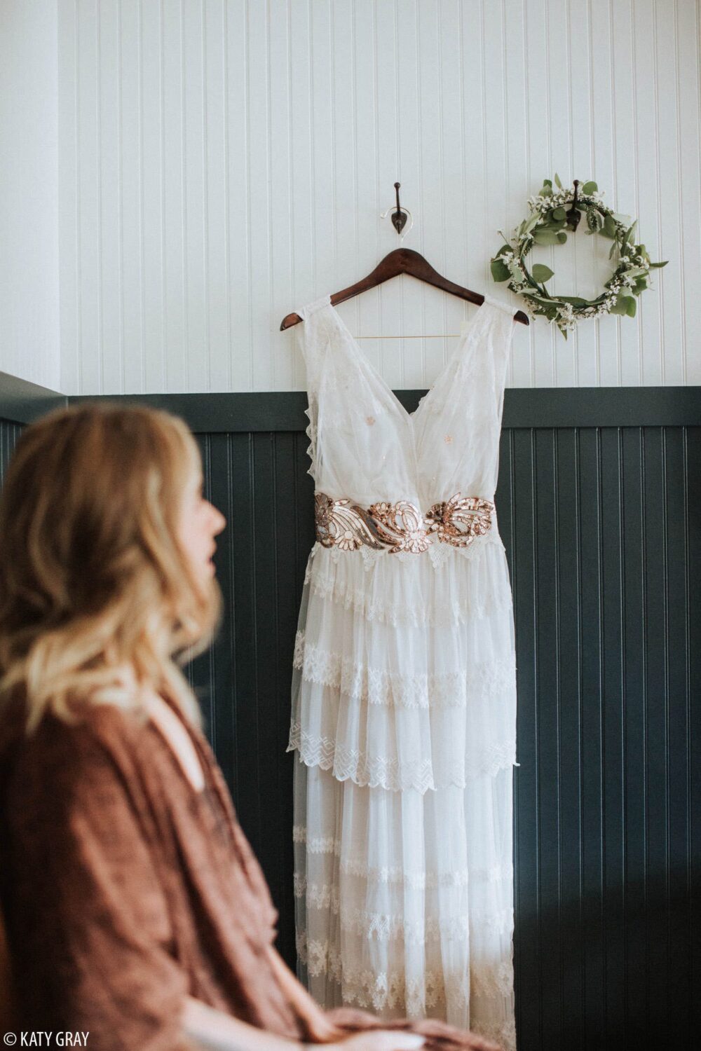 A bride with her wedding dress hanging on the wall, and a floral head crown.