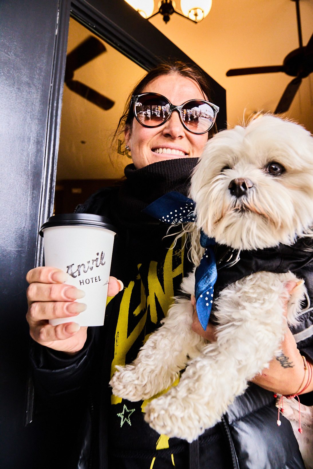 A woman holding her dog and a cup of coffee from Anvil Hotel.