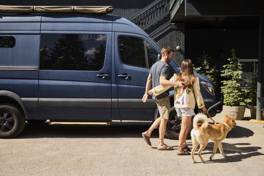 A couple with their dog, walking from their sprinter van to the Anvil Hotel lobby.